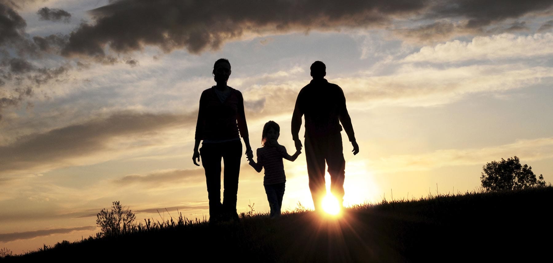 a silhouette of parents and a child walking toward a sunset