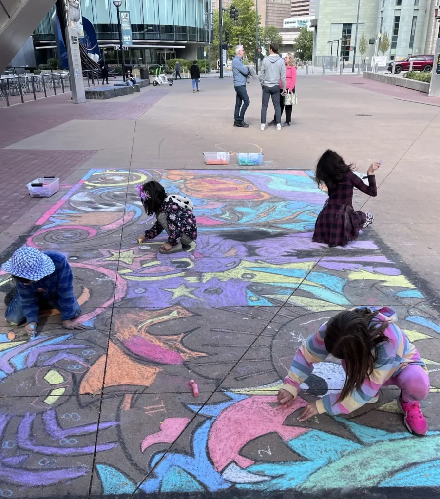 Kids coloring with chalk in front of the Denver Art Museum during the Millionth Kid celebration sponsored by Bellco