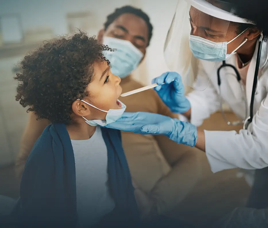 A child gets his mouth examined by a doctor during a checkup while his parent watches
