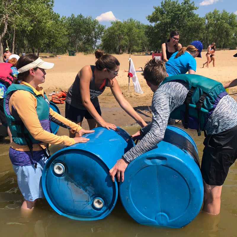 GFM|CenterTable team members building a raft out of barrels at a team building event with Outward Bound at Cherry Creek State Park